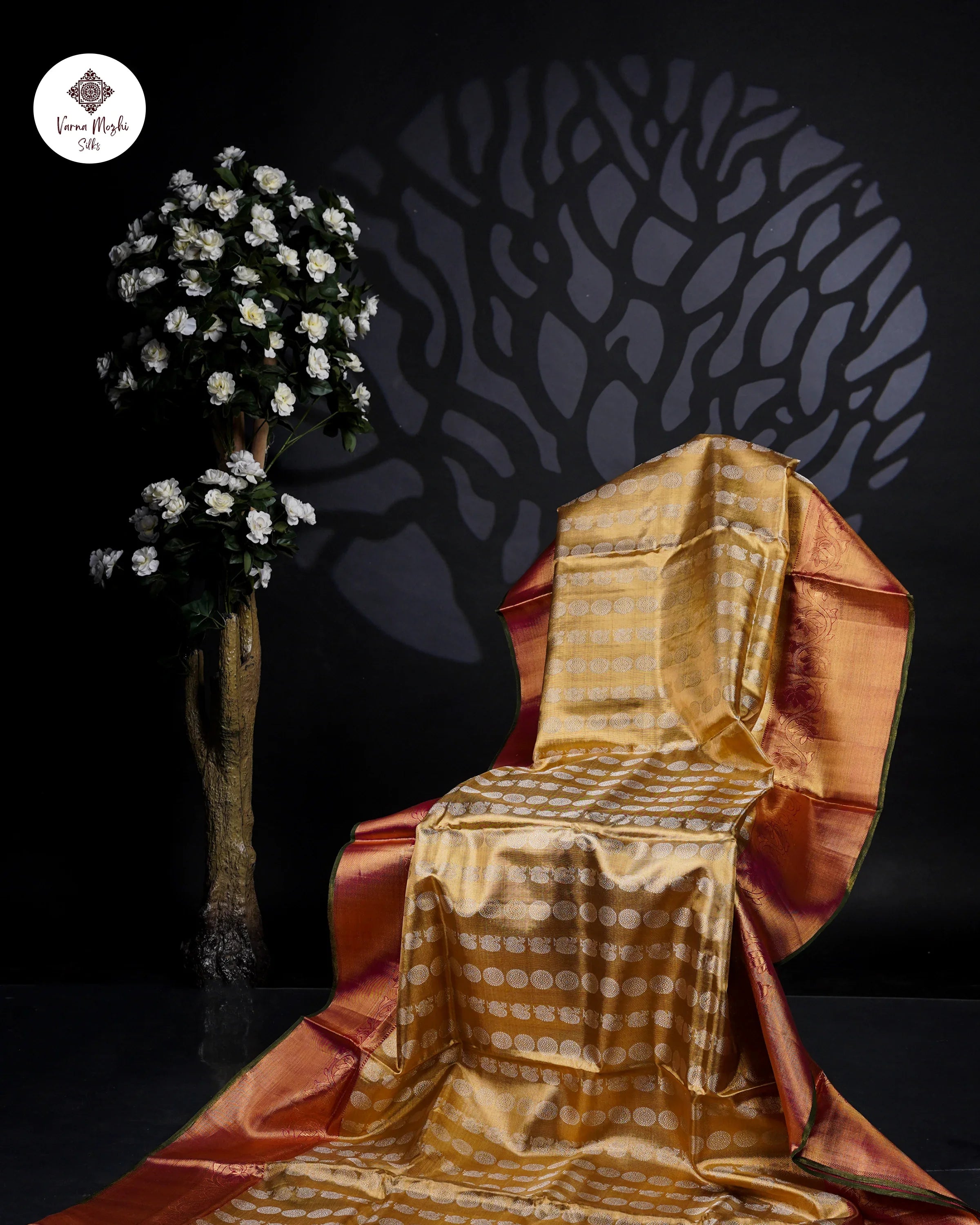 Golden Kanchipuram silk saree with zari butta pattern, rich border, displayed beside floral decor