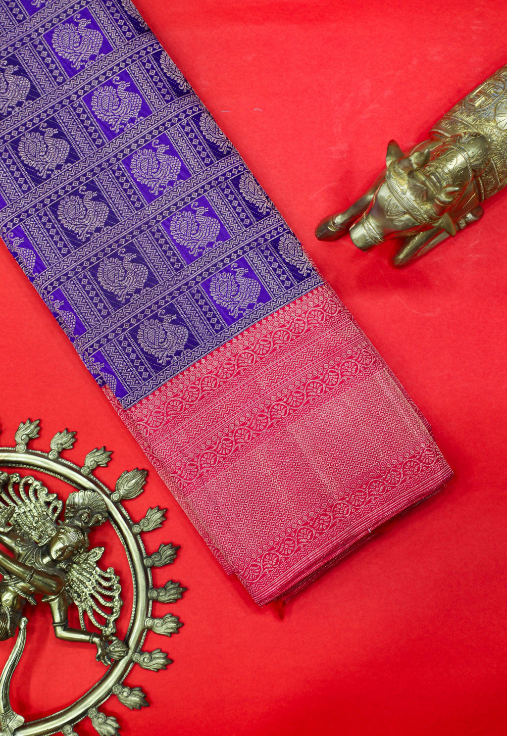 Purple and pink Kanchipuram silk saree with zari work, displayed with brass decor on red background